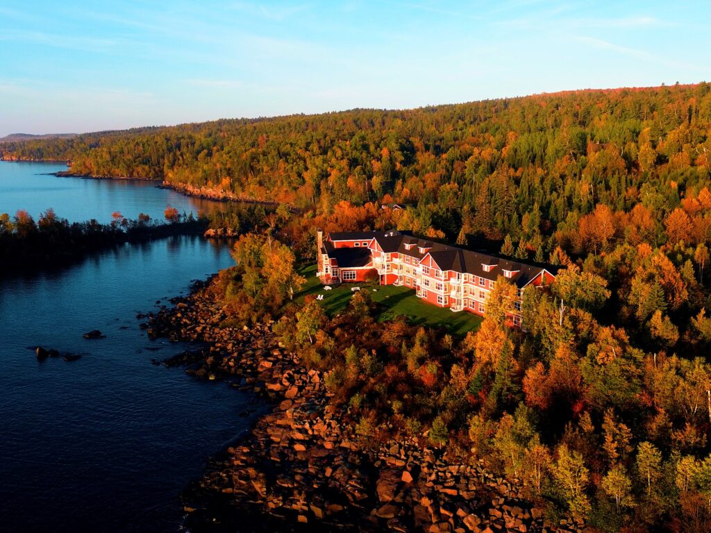Aerial view of Cove Point Lodge's red lodge building on the Lake Superior shoreline surrounded by peak fall color in Beaver Bay, Minnesota