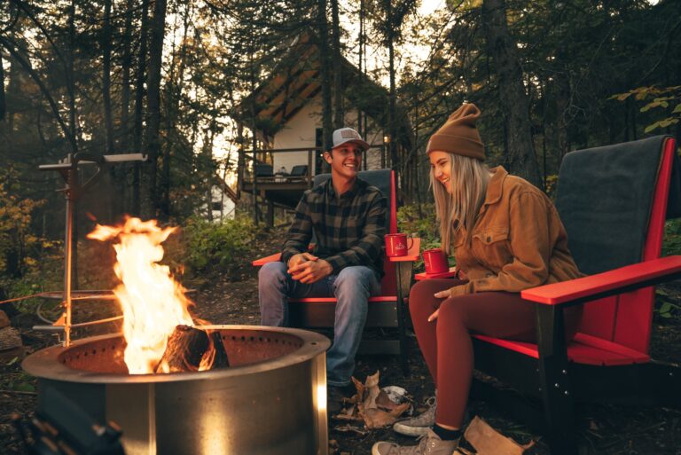 Two guests by a campfire in Adirondack chairs outside a cabin in the fall woods at North Shore Camping Co. in Beaver Bay, Minnesota