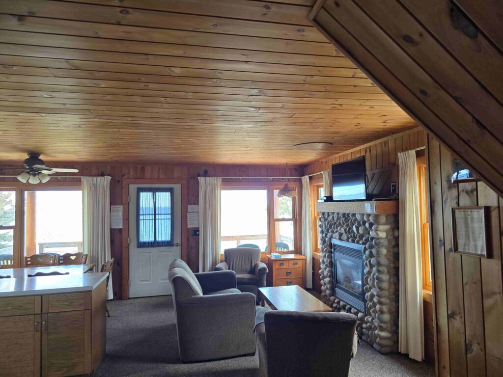 Knotty pine cabin interior at Ours Resort with a stone fireplace and windows facing Lake Superior